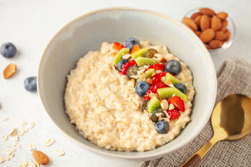 Oatmeal porridge with fruit and berries in bowl on the table. Homemade healthy breakfast cereal with strawberry, kiwi fruits, blueberry and almond