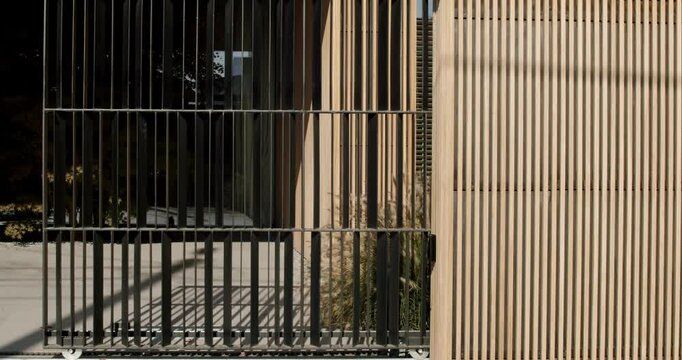 Modern house exterior with a sliding metal gate and wooden facade. Stylish design and architecture in a contemporary home. The secure entrance adds to the sense of privacy and exclusivity.