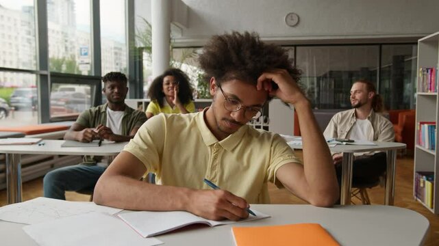 African American man student guy writing task in class lesson in classroom friends classmates bullying mocking bully throwing papers balls mockery laughing four students lecture in university college