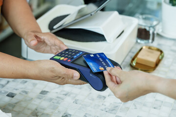 Closeup of terminal held at coffee shop counter while customer prepares to tap credit card,...