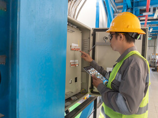 portrait of young asian male engineer wearing yellow helmet, glasses, vest doing inspection while...