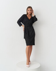 Elegant woman posing in a stylish black dress against a minimalist studio backdrop