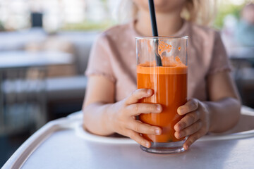 Fototapeta premium Close-up glass of fresh carrot juice in child hands