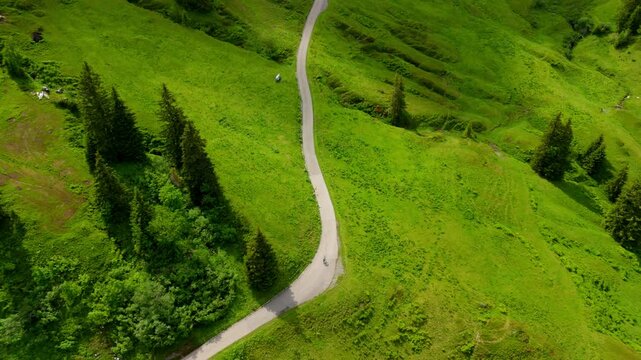 Cyclist pushes uphill on a gravel bike across serpentine mountain roads in Switzerland. Summer cycling tour in the Alps captured from above nature, endurance, and adventure in every frame. 
