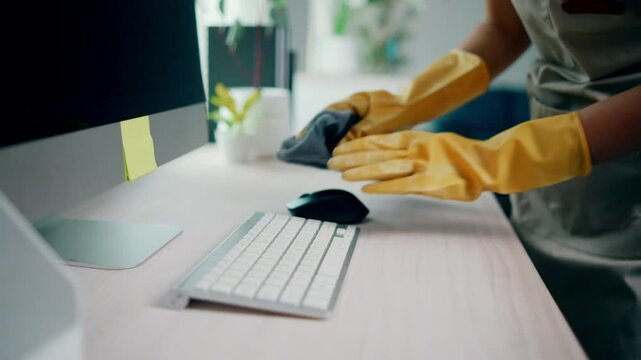 Detailed view of a professional cleaner wearing gloves while thoroughly disinfecting an office computer keyboard