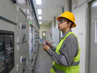 Portrait Asian Young Man, Working as an Engineer at a Power Plant Facility, Wearing a Work Jacket, Safety Glasses, and a Yellow Hard Hat. Electrical industry specialist Working on a Tablet Computer
