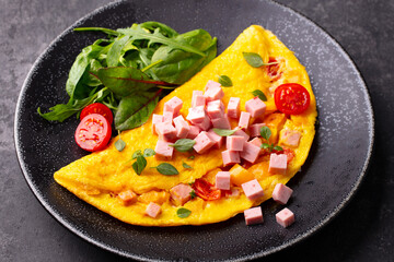 Omelet with cherry tomatoes, ham and green salad. Dark background. Close up.