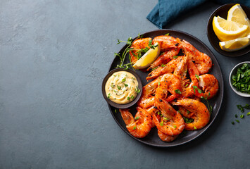 Grilled shrimp with lemon and sauce on a black plate. Grey background. Copy space. Top view.
