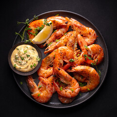 Grilled shrimp with lemon and sauce on a black plate. Dark background. Close up. Top view.