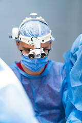Surgeon focused during complex procedure. Surgeon in a mask and glasses focuses intently in the...