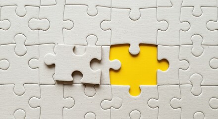 Fototapeta premium Close up of a white jigsaw puzzle with a missing piece revealing a yellow background, symbolizing completion, solution, and problem solving.