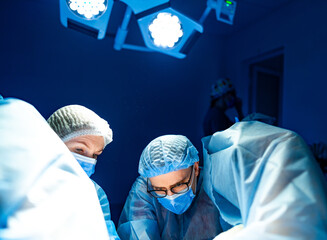 Surgeons working together sterilely. Doctors are conducting surgery under bright lights and wearing...