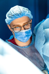 Surgeon focused on surgery. A surgeon in scrubs and a mask prepares for a crucial surgical...
