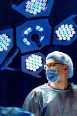 Surgeon readies for surgery. Surgeon in surgical attire looks around a well-lit operating room,...