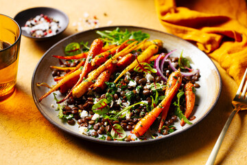 Warm salad. Roasted carrots with lentil, arugula and feta cheese. Yellow background. Close up.