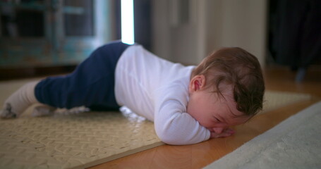 Baby lying face down on the floor, visibly upset and crying, expressing frustration and discomfort...