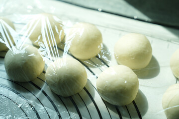 Round dough balls resting under plastic wrap, ready for baking or further preparation on a floured...