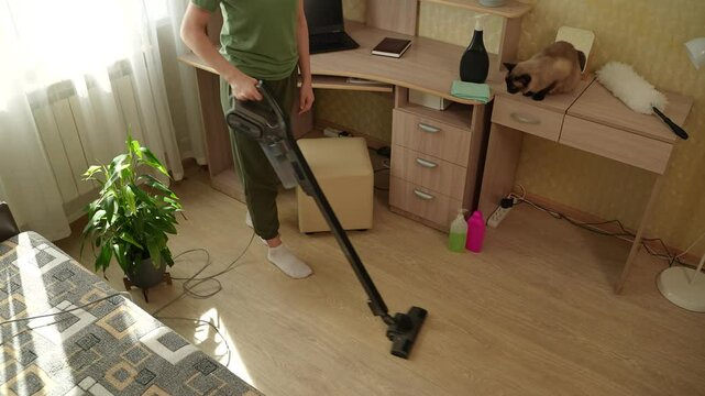Young blonde woman tidying up living room with vacuum cleaner, sunlight and fresh home decor. Vacuum cleaning the apartment to remove dust. A woman is tidying up the house.