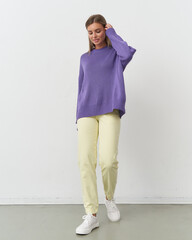 Model showcases vibrant purple sweater and light trousers in a chic studio setting