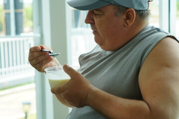 Fat Caucasian senior man with potbelly after workout hungry eating breakfast yoghurt,fruit salad healthy food and weight loss in fitness club. Health and wellness concept.