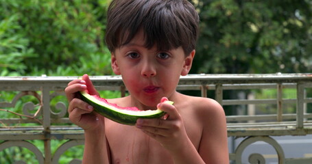 Young boy carefully eating a slice of watermelon, dripping juice as he enjoys the fresh and sweet fruit on a sunny day outdoors, savoring the moment