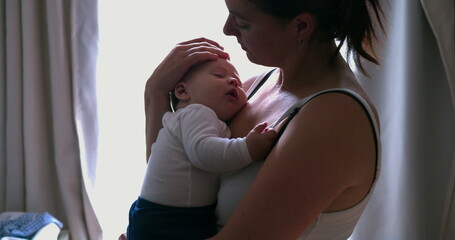 Tender moment of a mother cradling her sleeping infant, providing love and security in a quiet home setting, softly lit by natural light through the window
