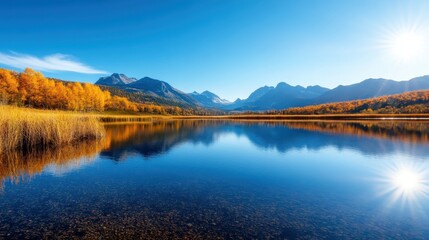 Fototapeta premium A captivating landscape showing a still lake reflecting golden autumn foliage and majestic mountains under a bright blue sky, exuding peace and tranquility.