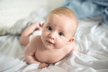 Portrait of a baby boy lying on a white bed. The child is 4 months old. Happy morning of the baby.