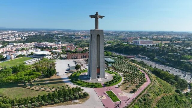 Aerial view of the Cristo Rei monument with urban landscape of Almada in the background, showing parks, roads, and residential areas