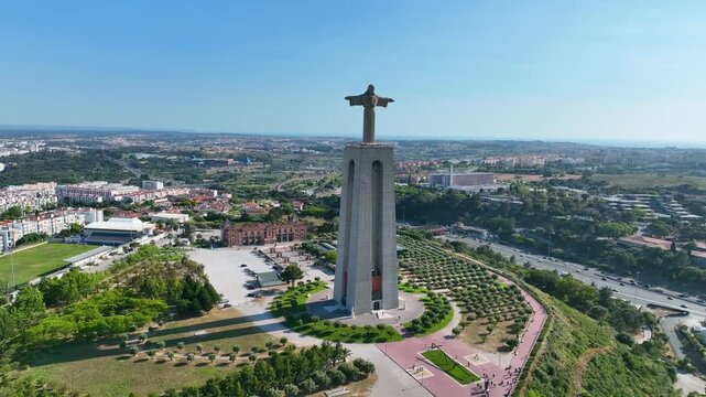 Aerial view of the Cristo Rei monument with urban landscape of Almada in the background, showing parks, roads, and residential areas