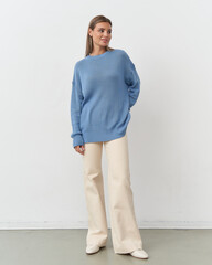 Elegant woman in a blue sweater and cream pants poses against a minimalist backdrop