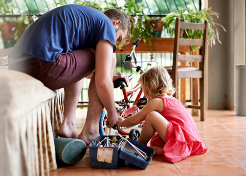 Man, kid and repair bicycle in home with help, support or DIY fix for child development. Father, young daughter or bike in living room for remove training wheels, toolbox or family bonding for growth