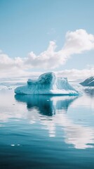 Iceberg reflecting on calm water, pristine blue ice, bright sunlight, and fluffy clouds