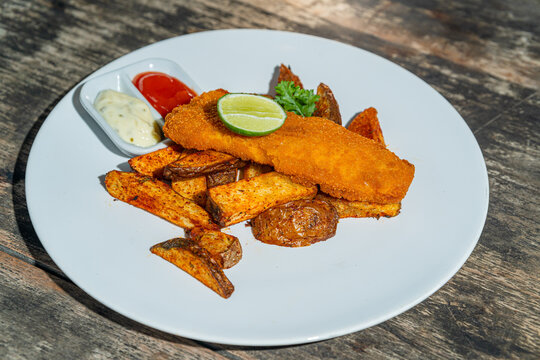 Deep fried fishs and chips, served with remoulade (sauce, mustard, herbs) on white plate. Isolated by wooden table. Food Photography