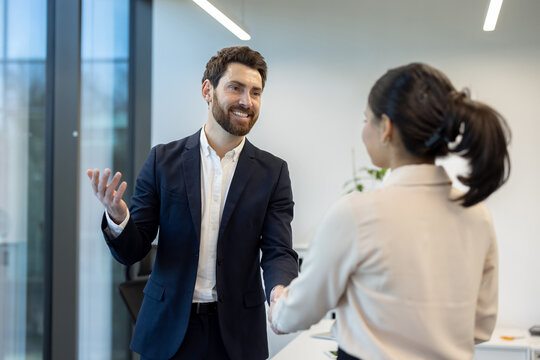A business professional is shaking hands with a colleague in a modern office setting. This portrays a collaborative work environment.
