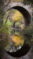 Naklejka premium Stone arch bridge over a tranquil reflecting pool.