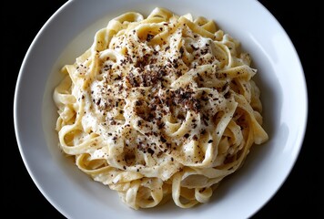 Creamy Fettuccine Pasta Dish with Shredded Cheese and Freshly Ground Black Pepper on a White Plate Against a Dark Background