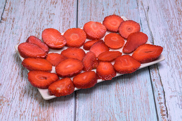 Fresh strawberry slices neatly arranged on a white plate over a rustic light blue wooden background. Top-down view, healthy and vibrant