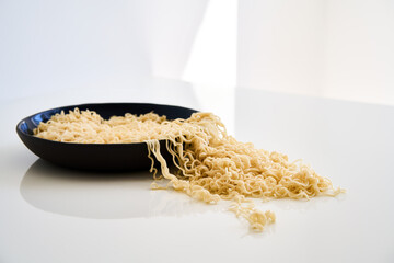 Cooked instant noodles overflow and spill from full bowl into table