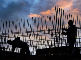 Silhouettes of construction workers working with steel reinforcement againts sunset sky