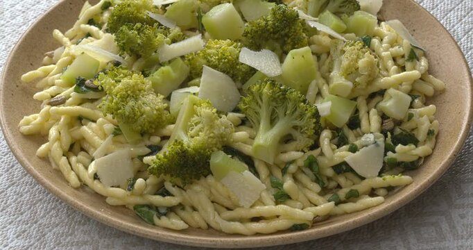 Trofie pasta with roughly chopped pesto, broccoli, and parmesan, background texture.