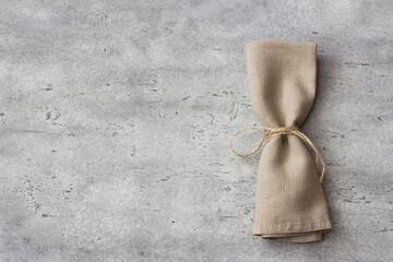Folded linen napkin tied with rope on gray stone background, rustic table decor, top view