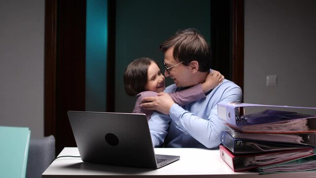 Businessman father is embracing his daughter affectionately while working late at night in his home office, demonstrating the challenges and joys of balancing work and family life