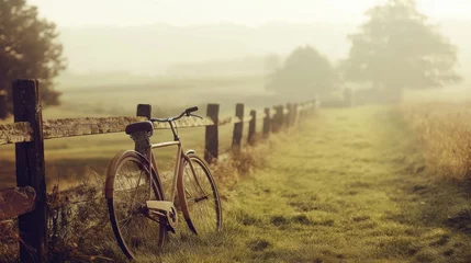 Fototapete Rustic bicycle resting beside a country fence in a misty field. © Prism Trail