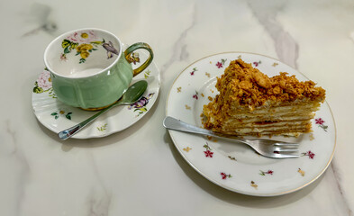 Elegant Tea Time: Slice of Napoleon Cake with Vintage Floral Teacup.Sweet Indulgence: Layered Cream...