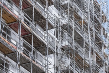 Close-up of scaffolding on a building under construction. The metal framework creates a complex geometric pattern against the building's facade.