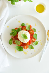 Salad Caprese with tomato, cherry, mozzarella and basil leaves on white wooden table