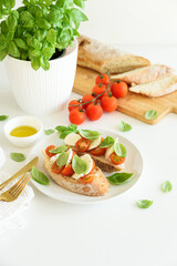 Bruschetta toasts with mozzarella, cherry tomato and basil leaves on white wooden table
