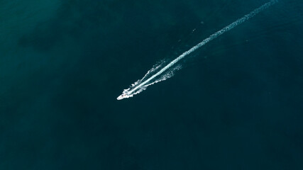 Fototapeta premium Aerial zenithal view of a motorboat crossing the blue sea. Its passage leaves a white trail on the surface of the water.