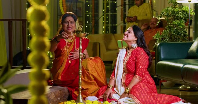 Lighting traditional samai with diya, Indian young girl in ethnic wear and senior mother joyfully celebrating Hindu festival Diwali in evening at home with festive decor and glowing diya illumination